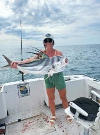 An angler proudly displaying a large Roosterfish aboard a fishing boat in open waters, showcasing a successful day of deep-sea fishing.