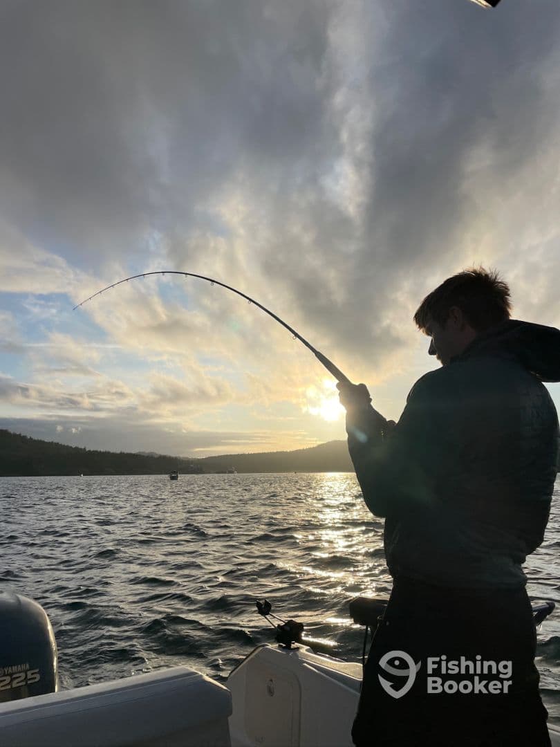 A young angler is reeling in a fish during a sunset fishing trip on a scenic lake, showcasing the excitement of the catch.