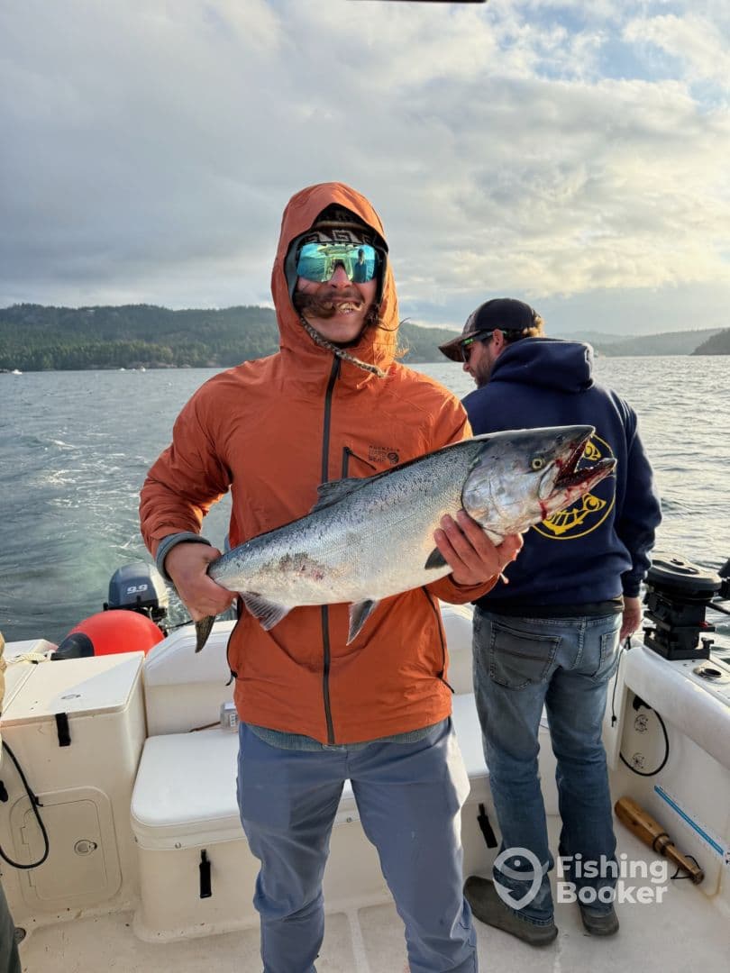An angler proudly displays a large Salmon while fishing on a boat in a scenic coastal environment.