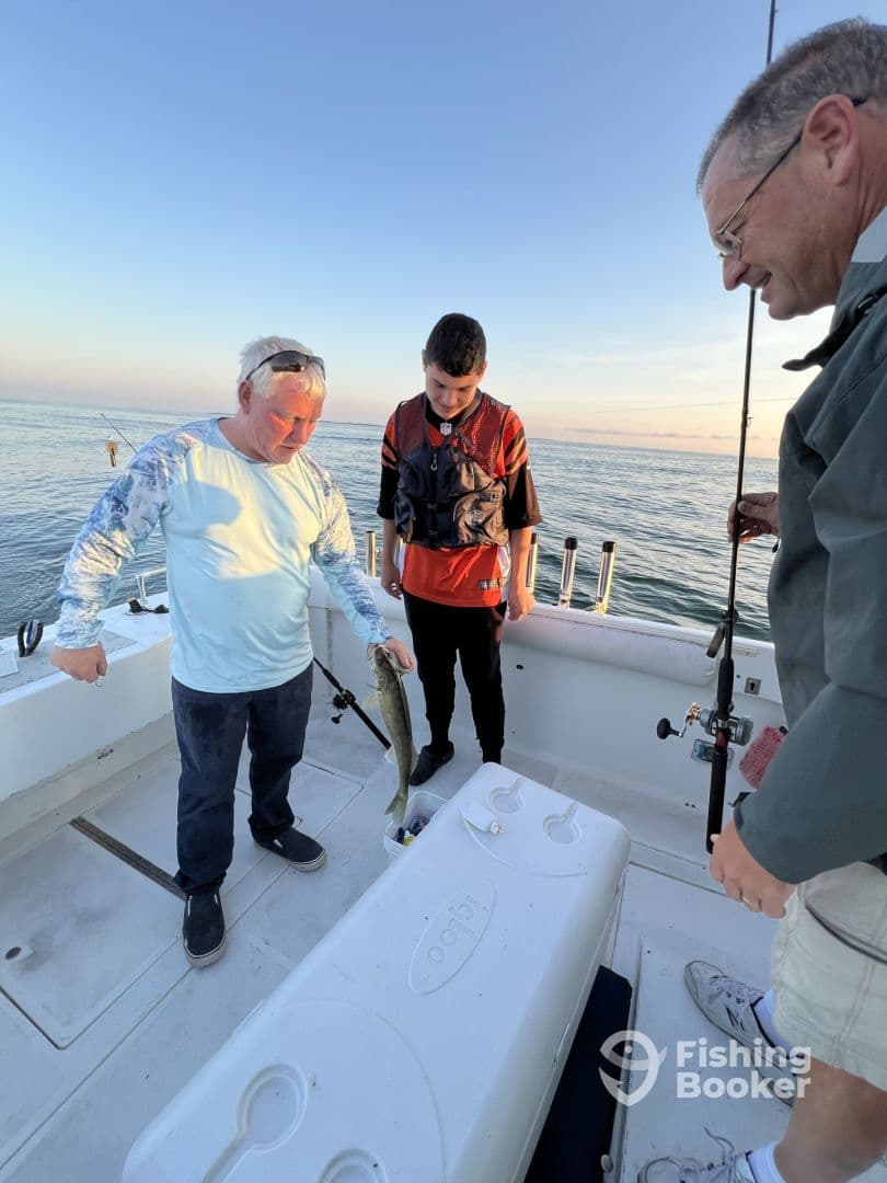 A young angler and an adult are displaying a caught fish on a fishing boat during a serene morning trip, showcasing a family fishing experience.