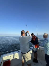 A young angler in a life jacket is reeling in a fish while two adults assist on a fishing charter in calm waters.