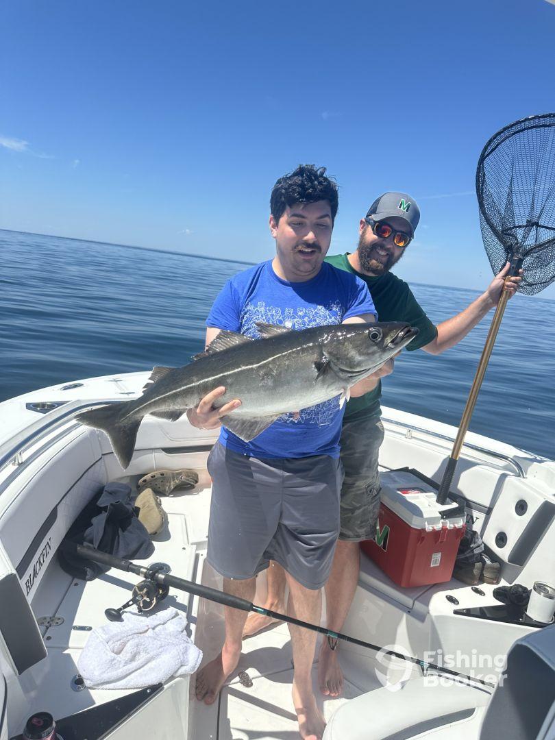 Two anglers proudly displaying a large fish on a boat during a sunny day on the water.