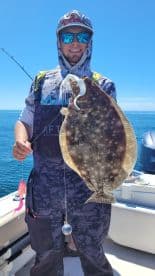 Angler proudly displaying a large Flounder while fishing on a boat, showcasing a successful catch in clear blue waters.