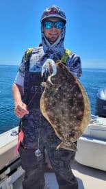 Angler proudly displaying a large Flounder while fishing on a sunny day, showcasing the vibrant blue waters.