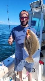 Angler proudly displaying a large Flounder while fishing on a sunny day.