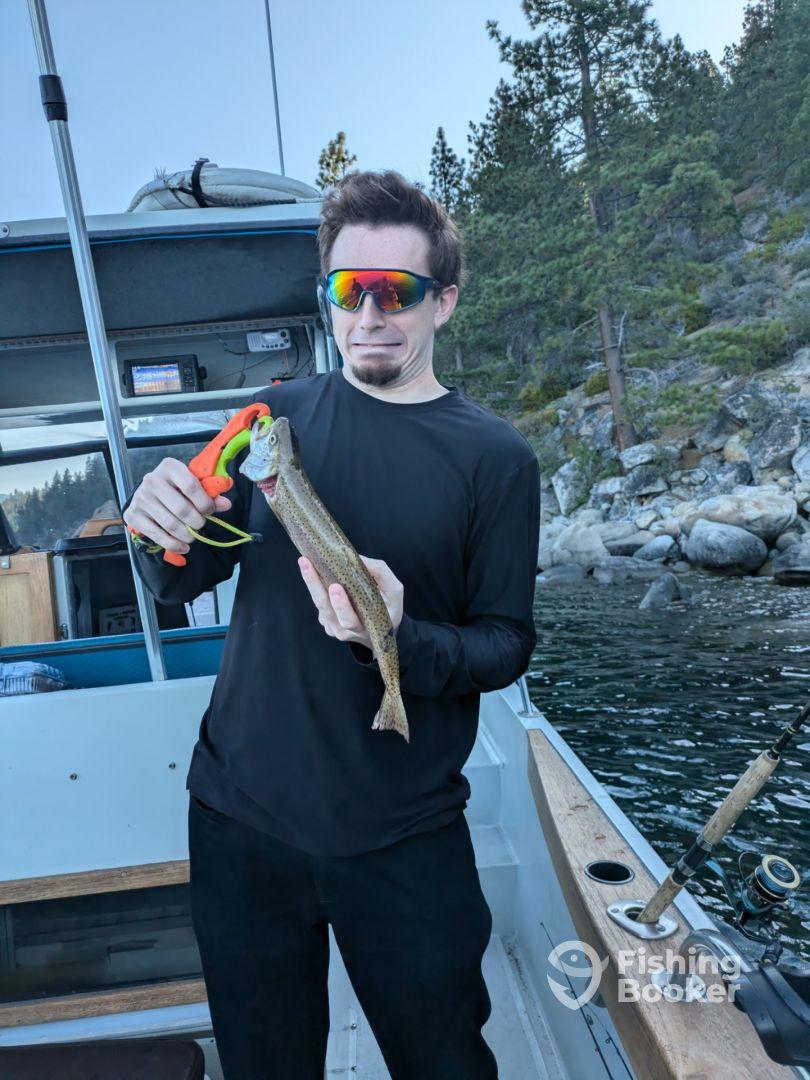 An angler holding a freshly caught trout while fishing from a boat in a scenic lake environment.