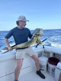An angler proudly displays a large Mahi Mahi aboard a fishing boat in open waters, showcasing a successful deep-sea fishing trip.