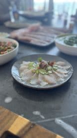 A beautifully arranged plate of fresh fish sashimi garnished with jalapeños and vegetables, showcasing the catch from a recent fishing trip.