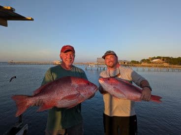 Two anglers proudly displaying their large Red Snapper catch at sunset, showcasing a successful fishing trip.