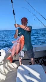 An angler proudly displaying a large Red Snapper while fishing on a boat in open waters.