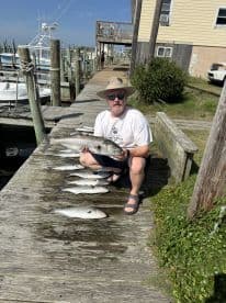 An angler proudly displaying a large fish alongside several others on a dock after a successful fishing trip.