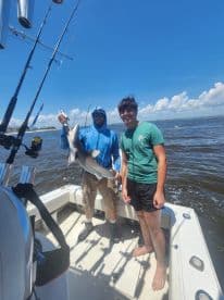 Two anglers on a boat proudly displaying a caught shark during a fishing trip.