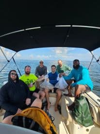 A group of six anglers on a boat, proudly displaying their catch in mesh bags during a fishing trip in open waters.