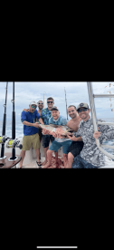 A group of six anglers proudly displaying a large Red Snapper on a fishing charter in open waters.