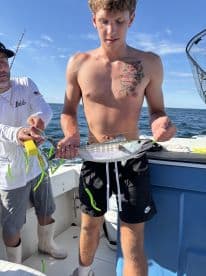 A young angler proudly displaying a freshly caught fish while fishing on a boat in open waters.