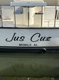 The exterior of the boat named 'Jus Cuz' is visible, docked in Mobile, AL, showcasing its sleek design and reflection in the water.