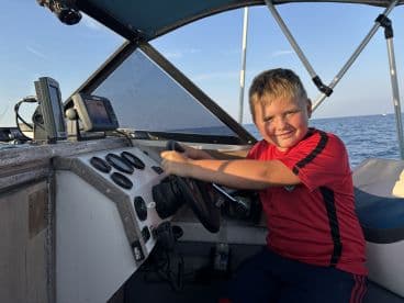 A young boy confidently steering the helm of a fishing boat, showcasing the interior features and electronics while enjoying a day on the water.