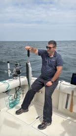 An angler proudly displaying a freshly caught fish aboard a fishing boat in open waters.