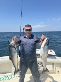 An angler proudly displaying two large Salmon while fishing offshore, showcasing a successful day on the water.