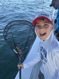 A young angler excitedly holding a net with a fish while fishing on a boat, showcasing the thrill of the catch.