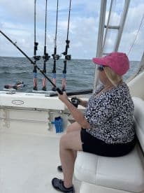 A woman fishing from the comfort of a well-equipped boat, showcasing multiple fishing rods ready for action on a sunny day at sea.
