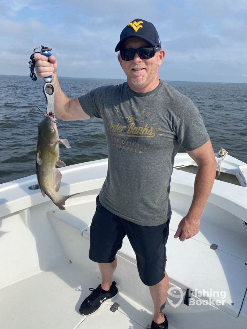 An angler proudly displaying a caught Catfish while aboard a fishing boat, enjoying a day on the water.