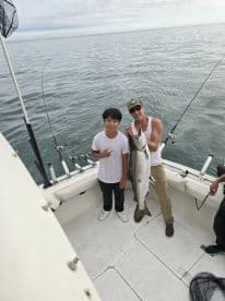 A young angler and an adult proudly display a large caught fish on a fishing boat, showcasing a successful day on the water.