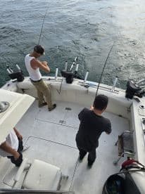 Two anglers actively fishing from the deck of a boat, engaged in reeling in their lines while surrounded by a calm sea.