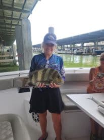 An angler proudly displaying a large Sheepshead fish on a boat, showcasing a successful fishing trip.