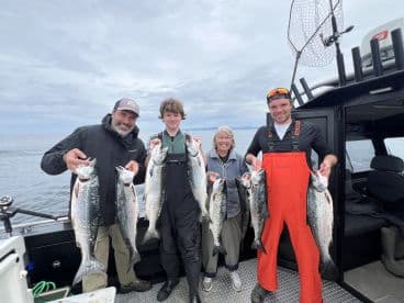 A family of four proudly displaying their catch of salmon while fishing on a boat in open waters.