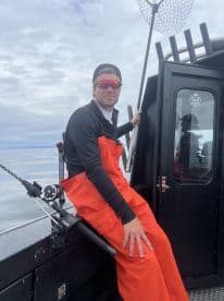 A young angler in bright orange fishing gear sits on the boat's interior, ready for a day of fishing on calm waters.