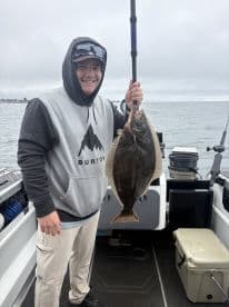 Angler proudly displaying a large Halibut while fishing from a boat, showcasing a successful day on the water.
