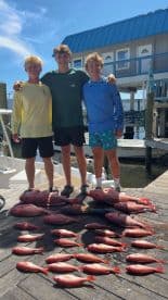 Three young anglers proudly displaying a successful catch of Red Snapper on the dock after a fishing trip.