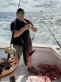 Angler proudly displaying a large Tuna on a sport fishing boat, showcasing the excitement of deep-sea fishing.