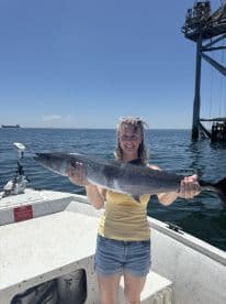 Angler proudly displaying a large King Mackerel while aboard a fishing boat in open waters.