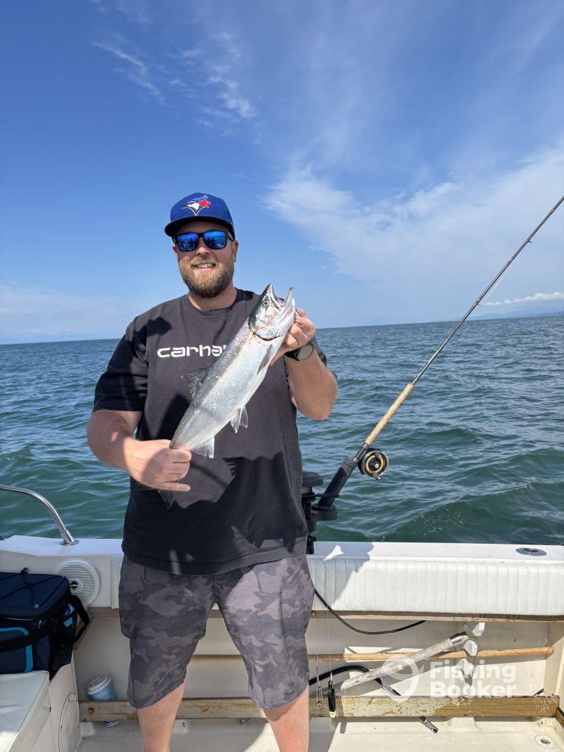 An angler proudly displaying a freshly caught Salmon while fishing on a boat, showcasing a beautiful day on the water.
