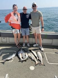 A group of three anglers proudly displaying their catch of multiple Salmon on a fishing boat, showcasing a successful day on the water.