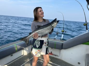 A proud angler holding a large Salmon while fishing on a boat, showcasing the excitement of a successful catch.