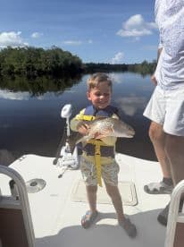 A young angler proudly displaying a Redfish while fishing on a calm river, showcasing a family-friendly fishing experience.