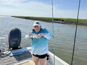 An excited angler holding a striped bass while fishing in a scenic coastal waterway, showcasing a successful catch during a sunny day.