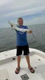 Young angler proudly holding a small shark while standing on a boat in open water.