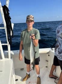 A young angler proudly displaying a large Spanish Mackerel while fishing on a boat in open waters.
