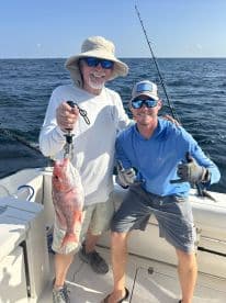 Two anglers proudly displaying a large Red Snapper while fishing on a boat in open waters.