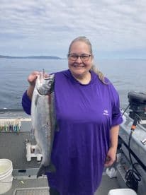 An angler proudly displaying a freshly caught Salmon while fishing on a scenic waterway.