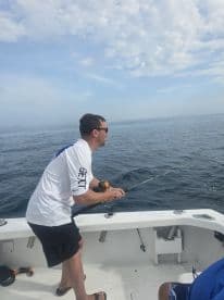 An angler actively reeling in a catch while fishing on a boat in open waters, showcasing the excitement of the sport.