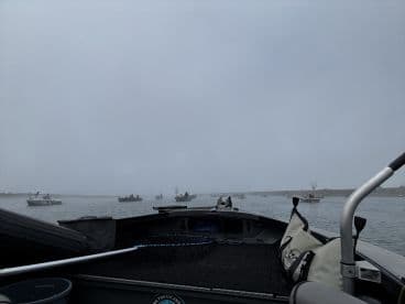 View from inside a fishing boat on a foggy day, showcasing multiple boats in the distance, likely engaged in fishing activities.
