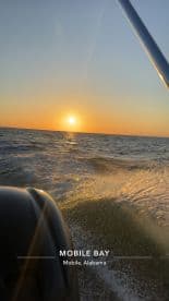 A scenic view of Mobile Bay at sunset, showcasing the boat's engine and the shimmering water.