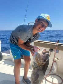 A young angler joyfully holding a large Grouper while fishing offshore, showcasing a successful day on the water.
