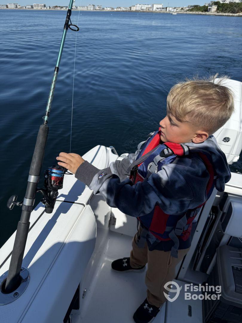 A young angler is focused on reeling in a catch while fishing from a boat in calm waters, showcasing the excitement of fishing.
