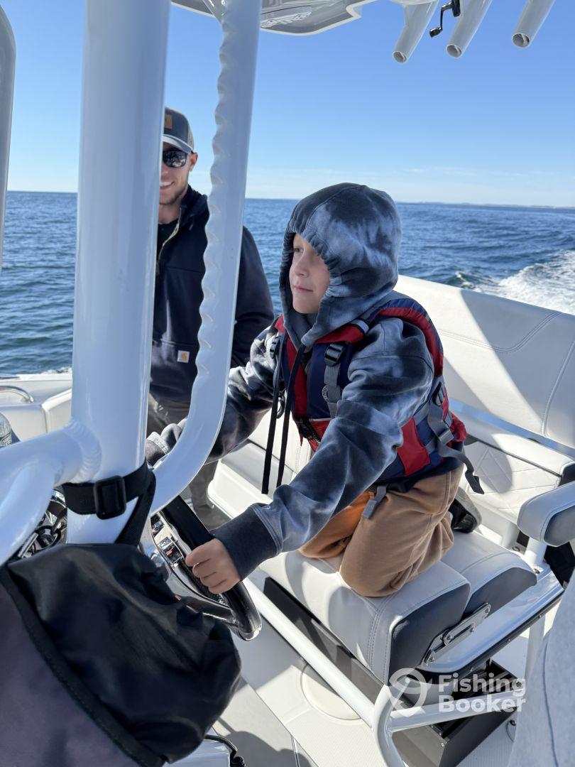 A young boy confidently steering the boat while an adult supervises, showcasing a fun family fishing experience on the water.